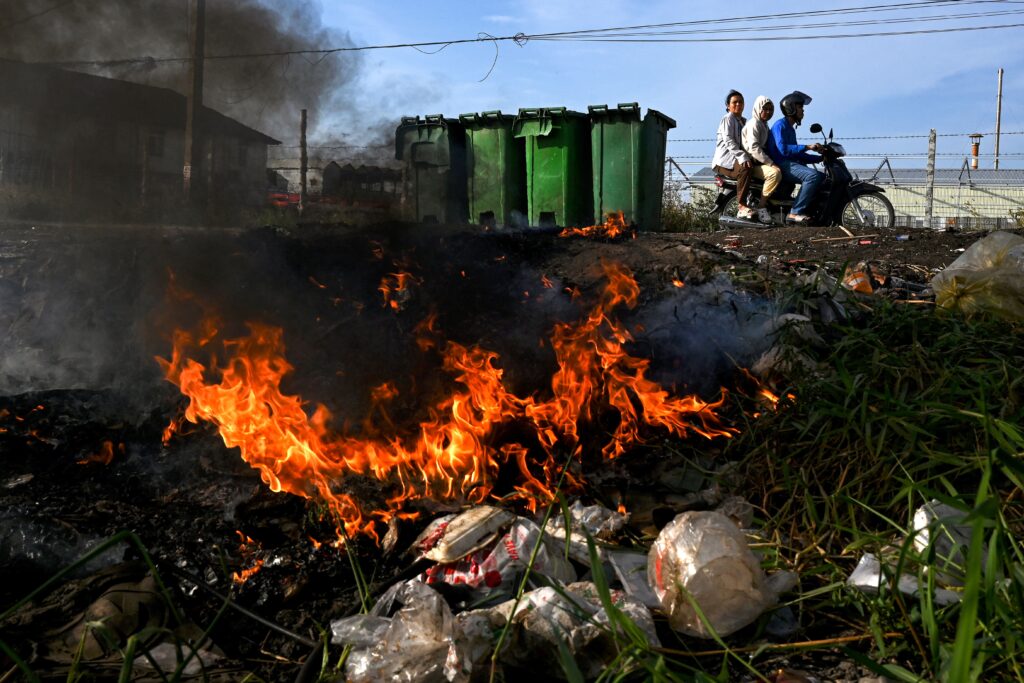 Discarded plastic burns in a field.