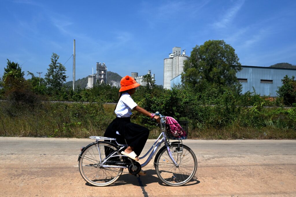 A girl in school uniform cycles past the cement kiln.