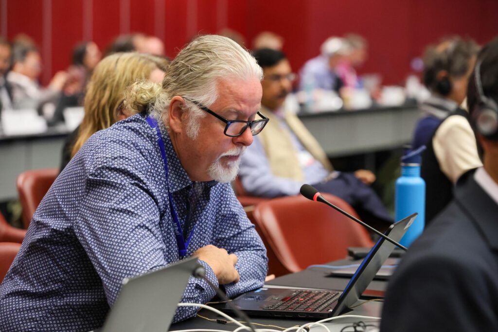 Lee Bell leans over a laptop and a microphone at an international negotiations.